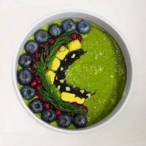 A vibrant green smoothie bowl decorated with blueberries and garnishes for a healthy breakfast.